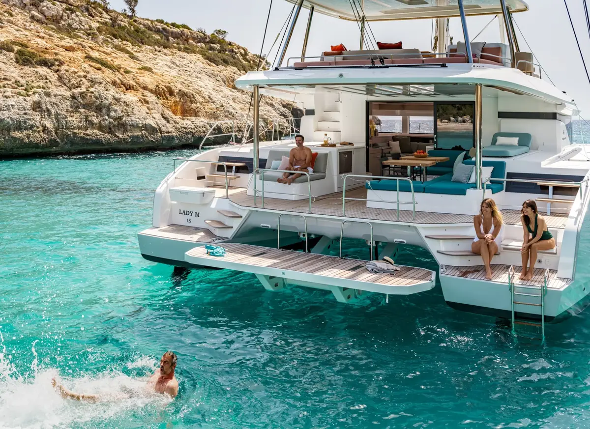 Lagoon 55 catamaran anchored in turquoise water with guests swimming off the stern