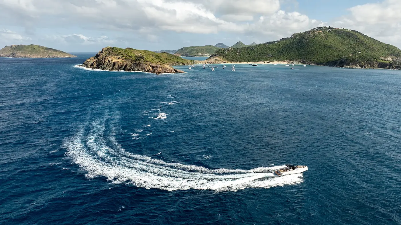 Boat leaving a wake in deep blue water off a green St Barts headland